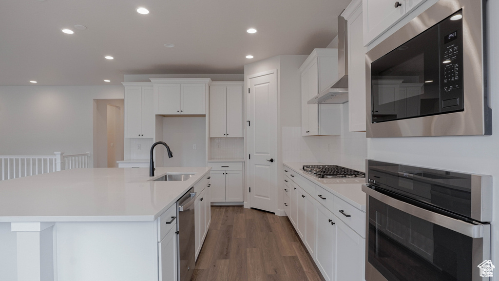 Kitchen featuring appliances with stainless steel finishes, wood finished floors, recessed lighting, white cabinetry, and an island with sink