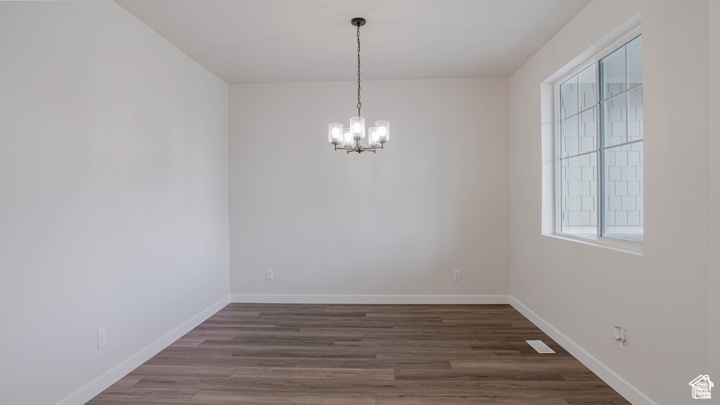 Unfurnished room with a chandelier, plenty of natural light, and dark wood-type flooring