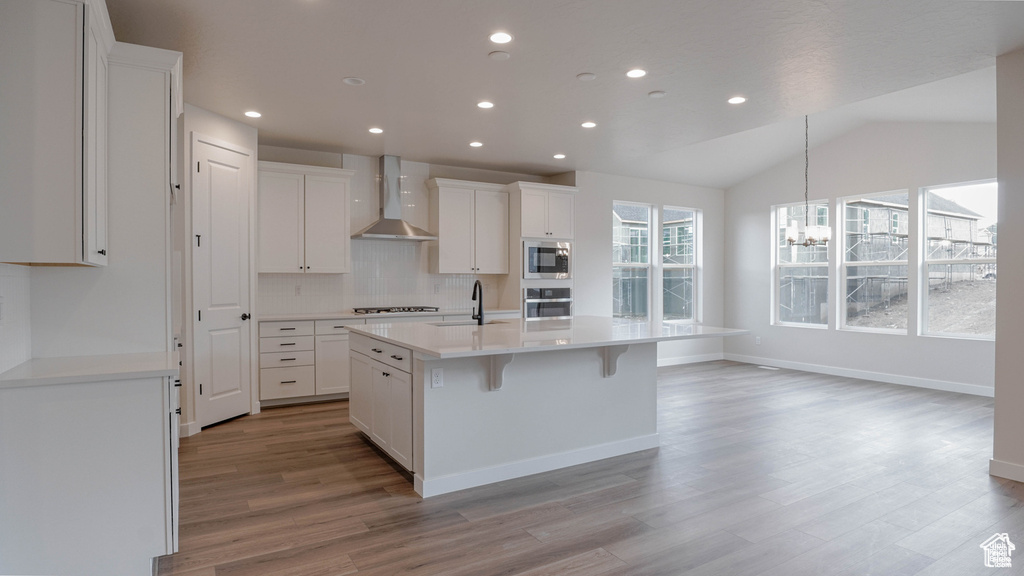 Kitchen with wall chimney exhaust hood, appliances with stainless steel finishes, a chandelier, light wood-type flooring, and tasteful backsplash
