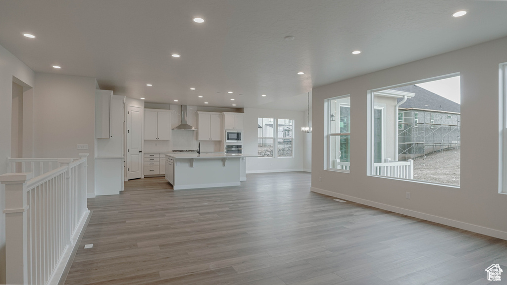 Kitchen with wall chimney exhaust hood, open floor plan, light wood-style floors, white cabinetry, and recessed lighting