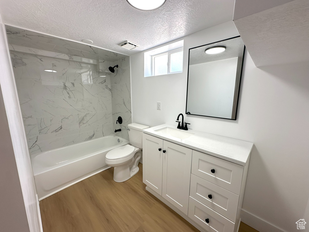 Full bathroom with a textured ceiling, vanity, wood finished floors, and bathtub / shower combination