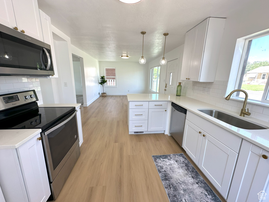 Kitchen with appliances with stainless steel finishes, white cabinetry, light wood-style floors, a peninsula, and backsplash