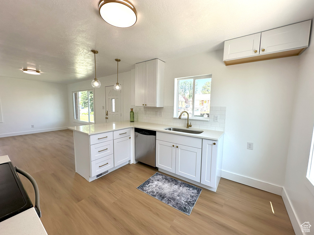 Kitchen with stainless steel dishwasher, black range, a peninsula, light wood-style floors, and a textured ceiling