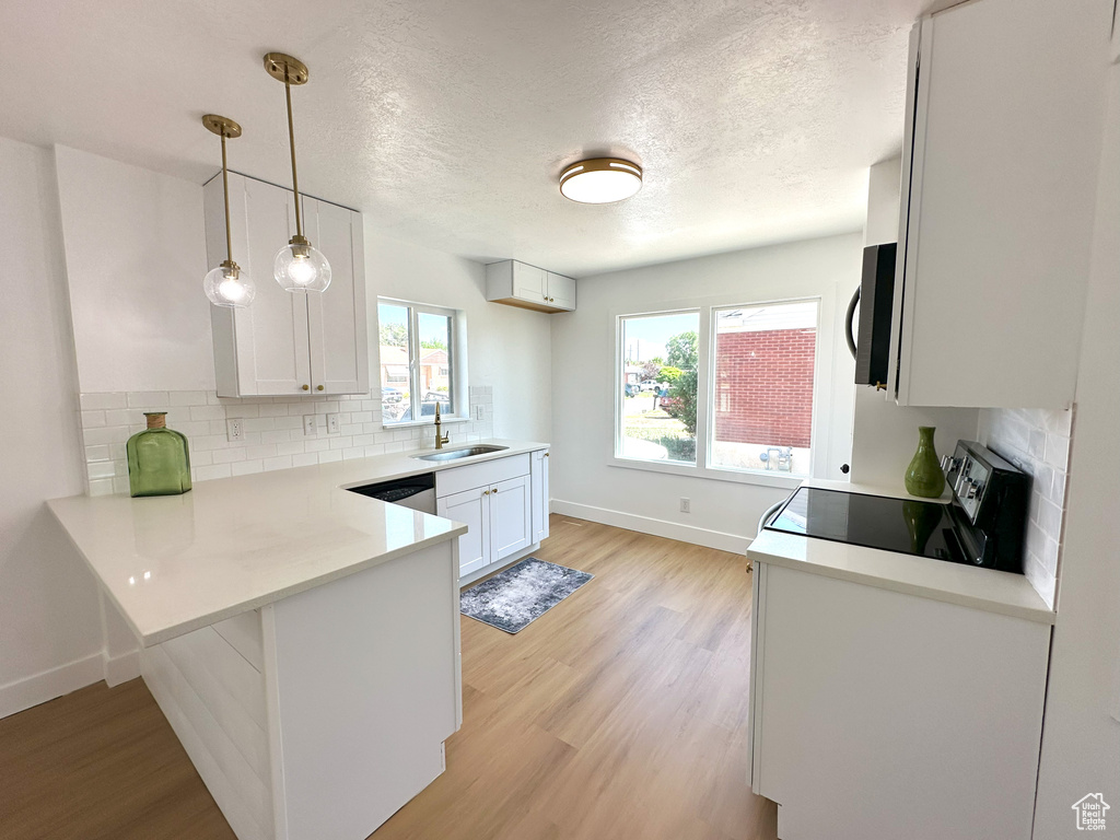 Kitchen with a peninsula, stainless steel appliances, light wood-type flooring, decorative backsplash, and a textured ceiling