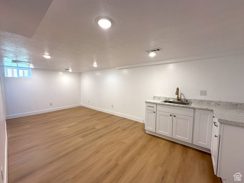 Below grade area with light wood-style flooring and a textured ceiling