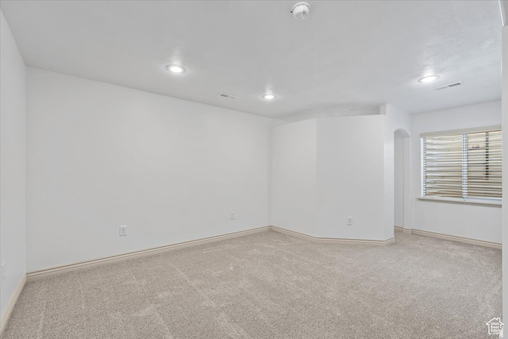 Carpeted spare room with a smoke detector, arched walkways, and recessed lighting