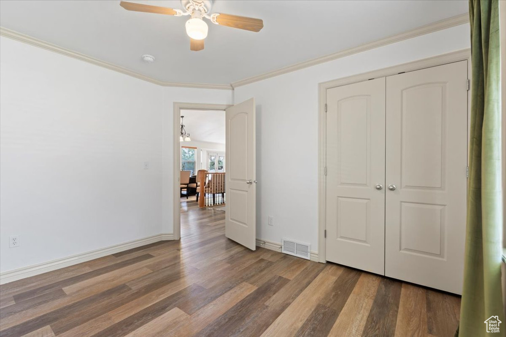 Unfurnished bedroom with wood finished floors, crown molding, a ceiling fan, and a closet