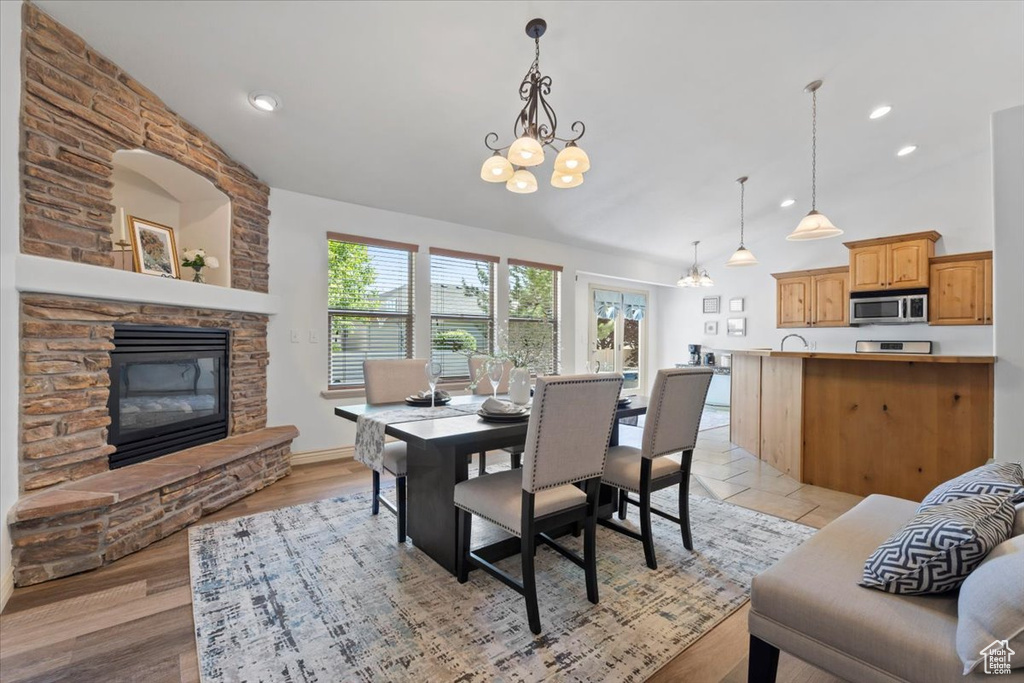 Dining area featuring vaulted ceiling, a chandelier, a fireplace, recessed lighting, and light wood-style flooring