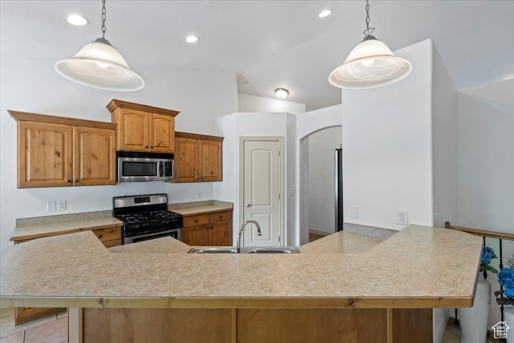 Kitchen featuring stainless steel appliances, vaulted ceiling, a peninsula, light countertops, and decorative light fixtures