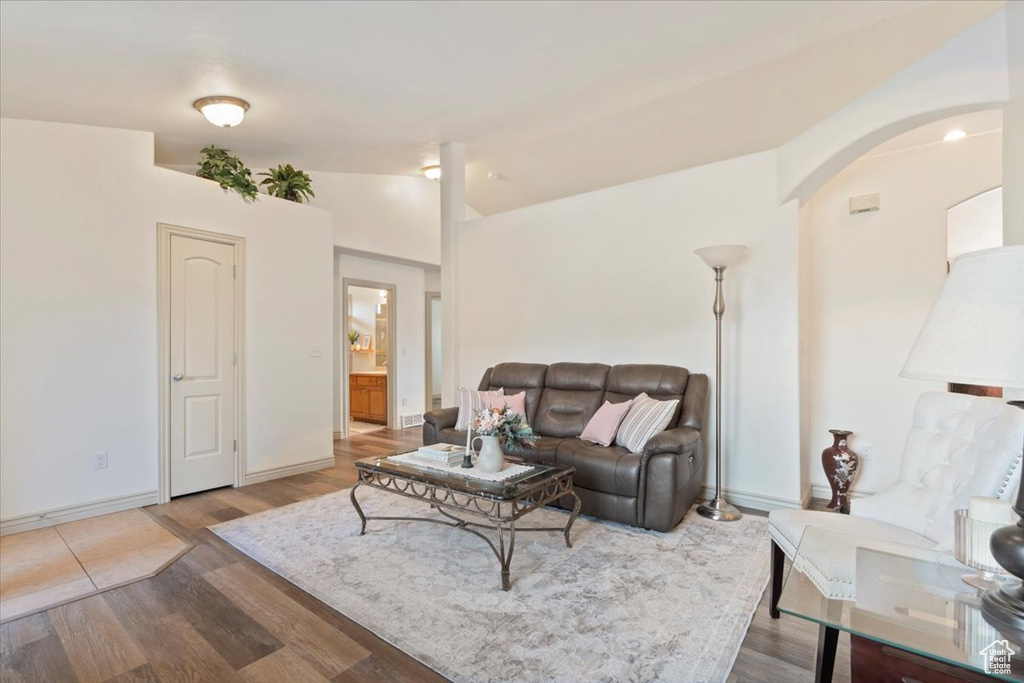 Living room featuring wood finished floors, vaulted ceiling, and arched walkways