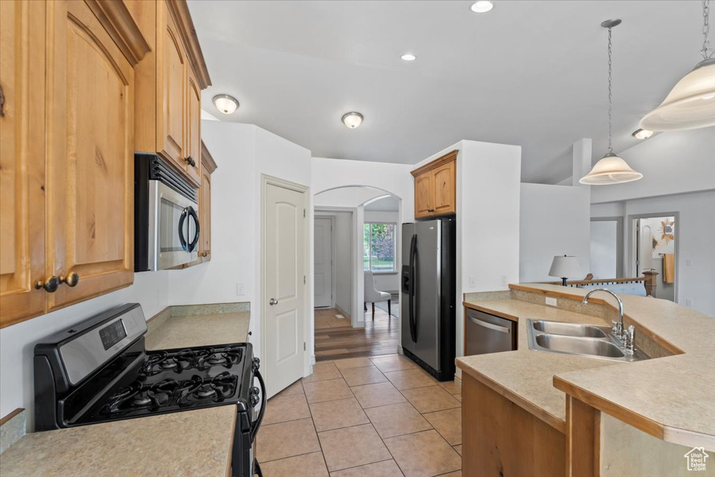 Kitchen with appliances with stainless steel finishes, arched walkways, light countertops, pendant lighting, and recessed lighting