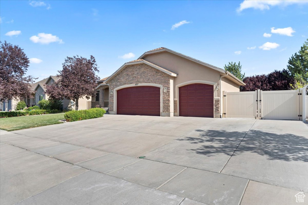 View of front of house with a gate, an attached garage, concrete driveway, stone siding, and stucco siding