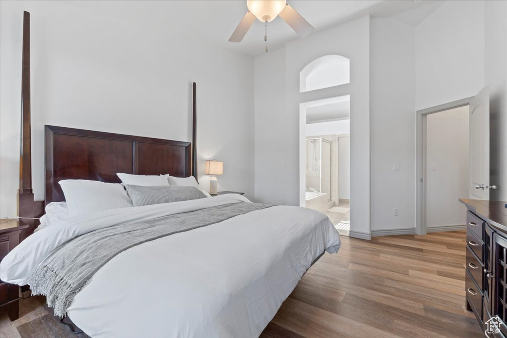 Bedroom with light wood finished floors, a towering ceiling, ensuite bath, and a ceiling fan