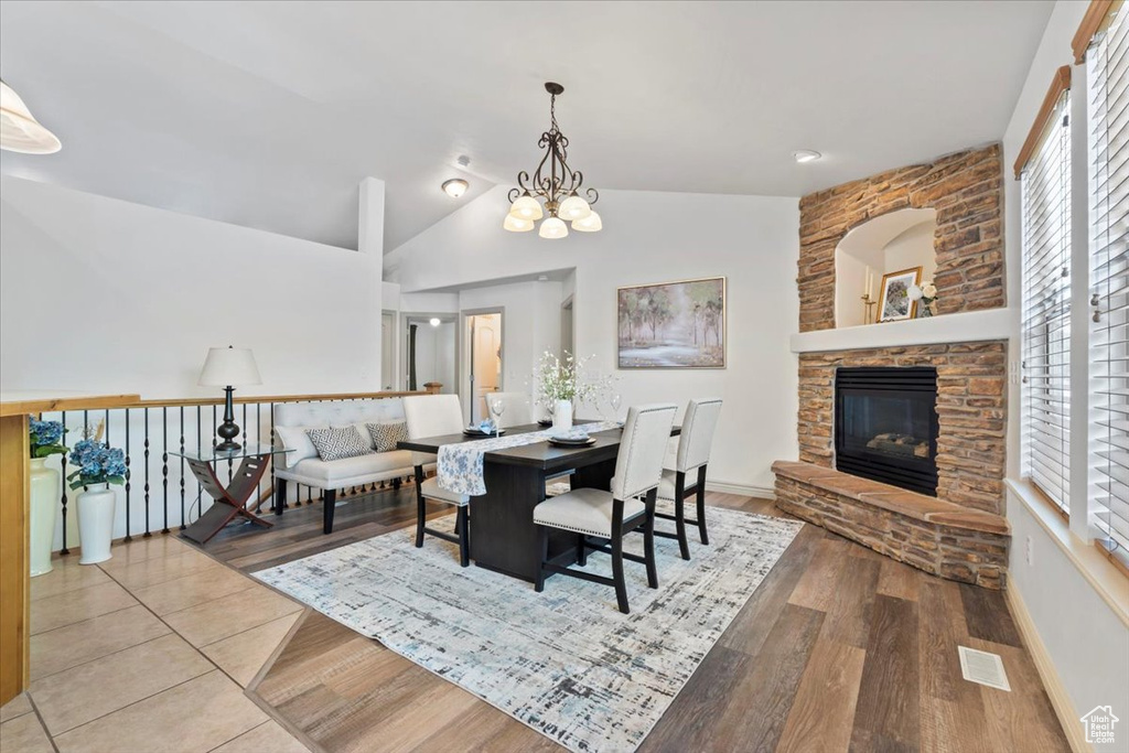 Dining room featuring lofted ceiling, a fireplace, wood finished floors, and a chandelier