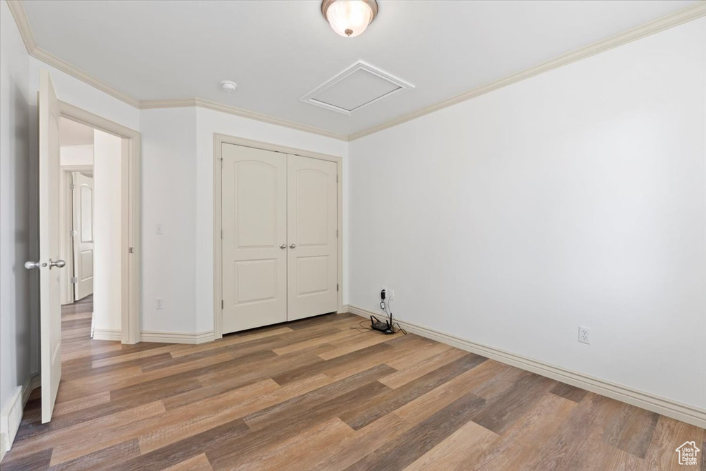 Unfurnished bedroom featuring wood finished floors, attic access, a closet, and crown molding