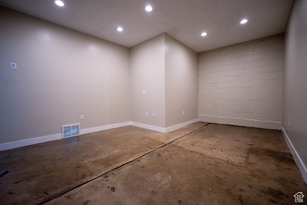 Empty room with unfinished concrete flooring, recessed lighting, and concrete block wall