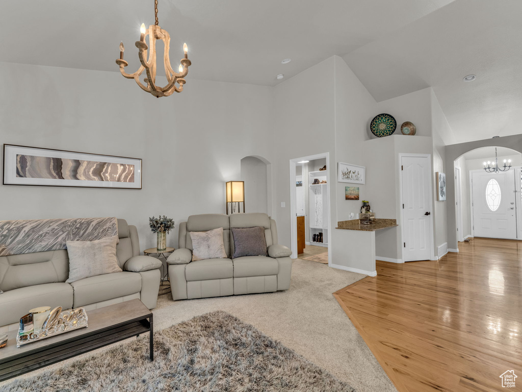Living room featuring arched walkways, a chandelier, high vaulted ceiling, and light wood finished floors