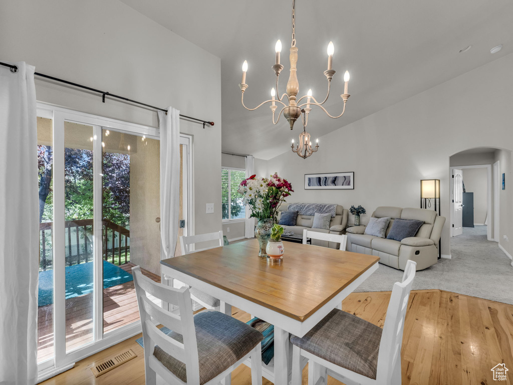 Dining space with arched walkways, a chandelier, a towering ceiling, and light wood-style flooring