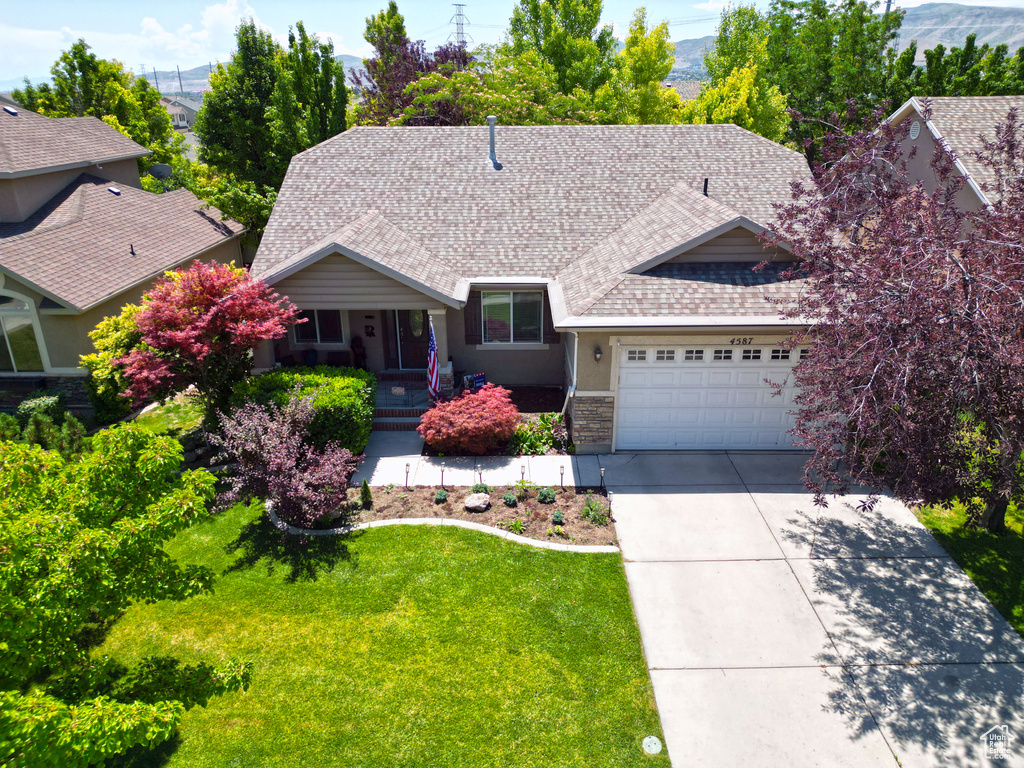 View of front of house with driveway, a garage, a front lawn, roof with shingles, and stone siding