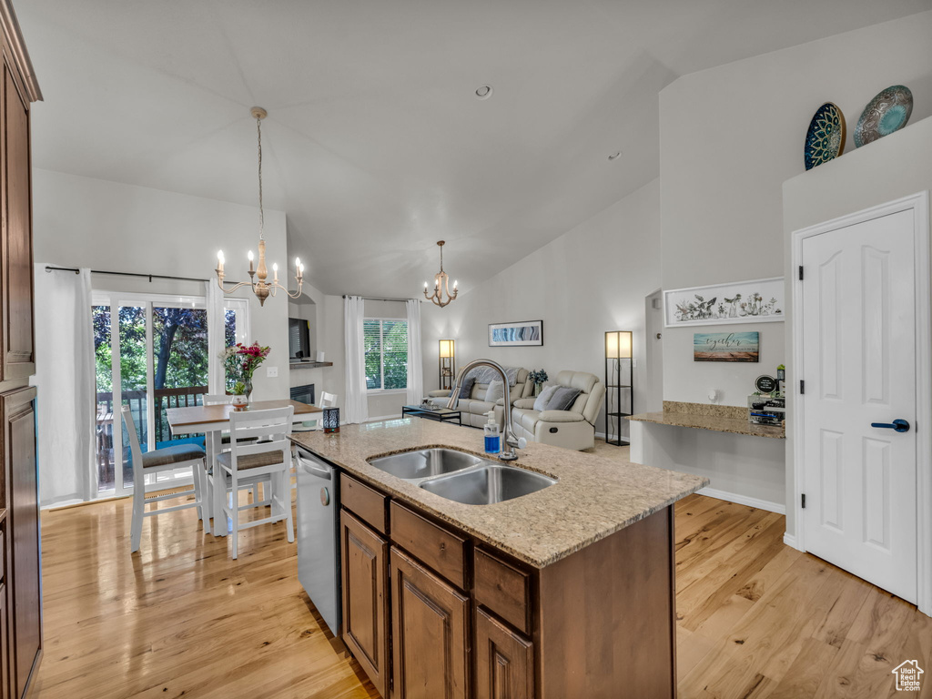 Kitchen featuring stainless steel dishwasher, a chandelier, a kitchen island with sink, light wood finished floors, and brown cabinetry