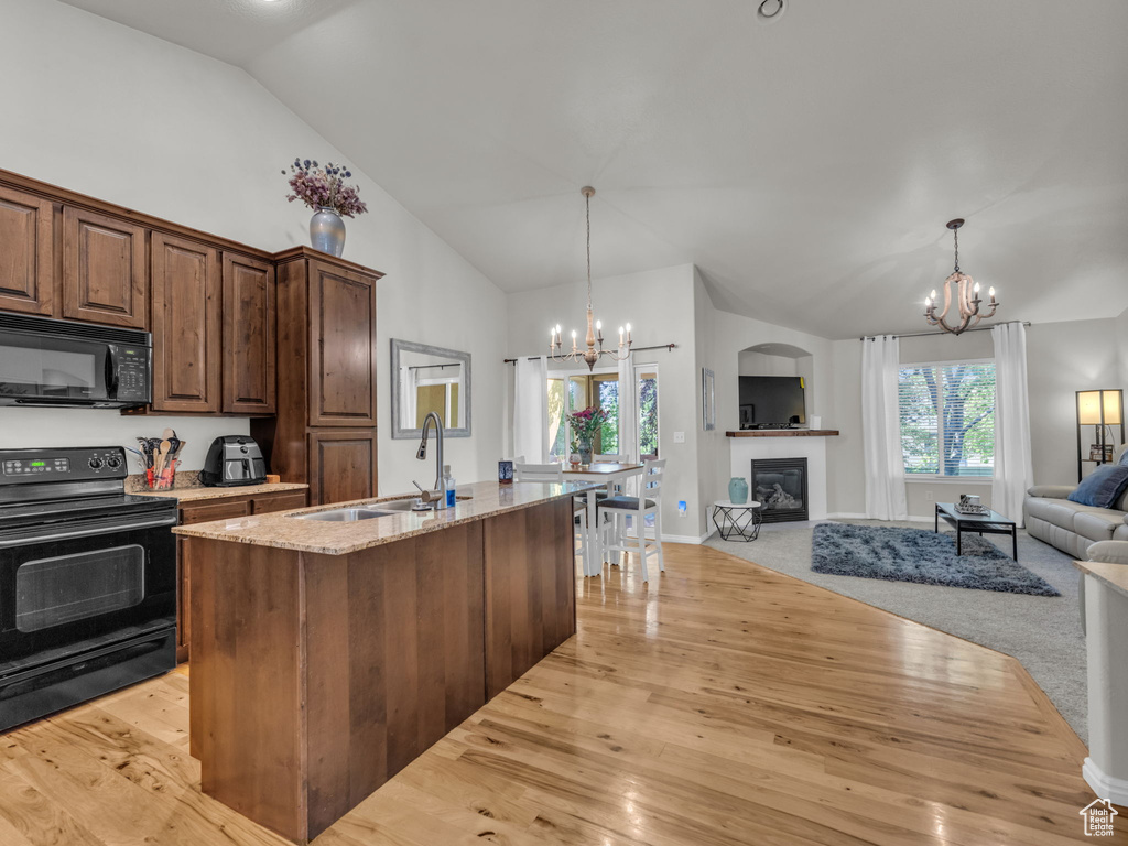 Kitchen featuring black appliances, a chandelier, open floor plan, light wood-style floors, and high vaulted ceiling