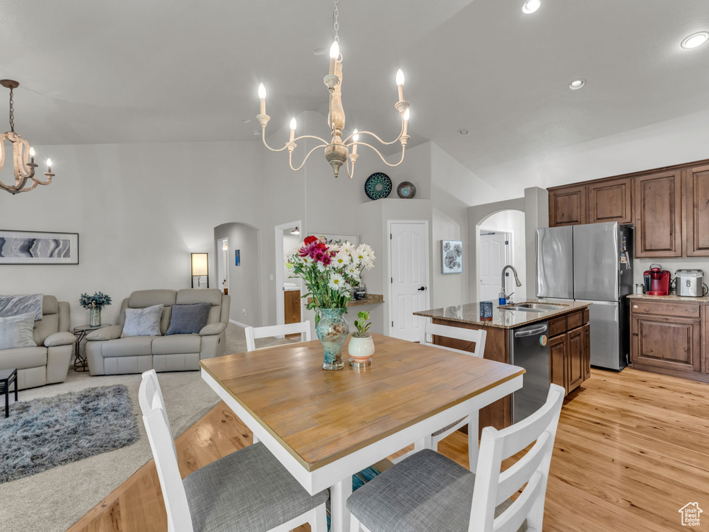 Dining area with a chandelier, arched walkways, light wood-style flooring, high vaulted ceiling, and recessed lighting