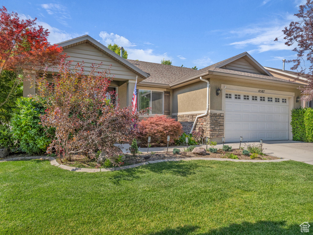 Ranch-style house with stucco siding, an attached garage, stone siding, roof with shingles, and a front lawn
