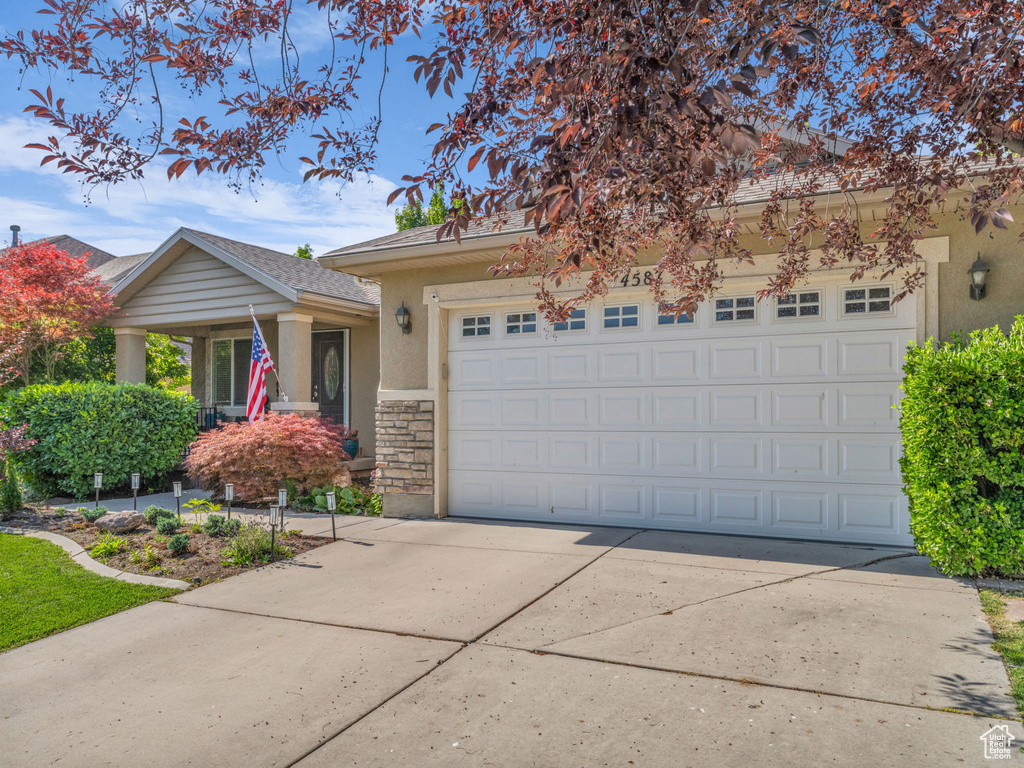 View of front of property with driveway, stone siding, an attached garage, and stucco siding