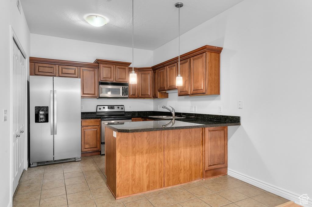 Kitchen with stainless steel appliances, a peninsula, brown cabinets, and light tile patterned floors