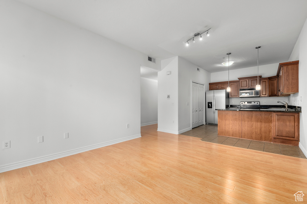 Kitchen with appliances with stainless steel finishes, dark countertops, a peninsula, light wood finished floors, and hanging light fixtures