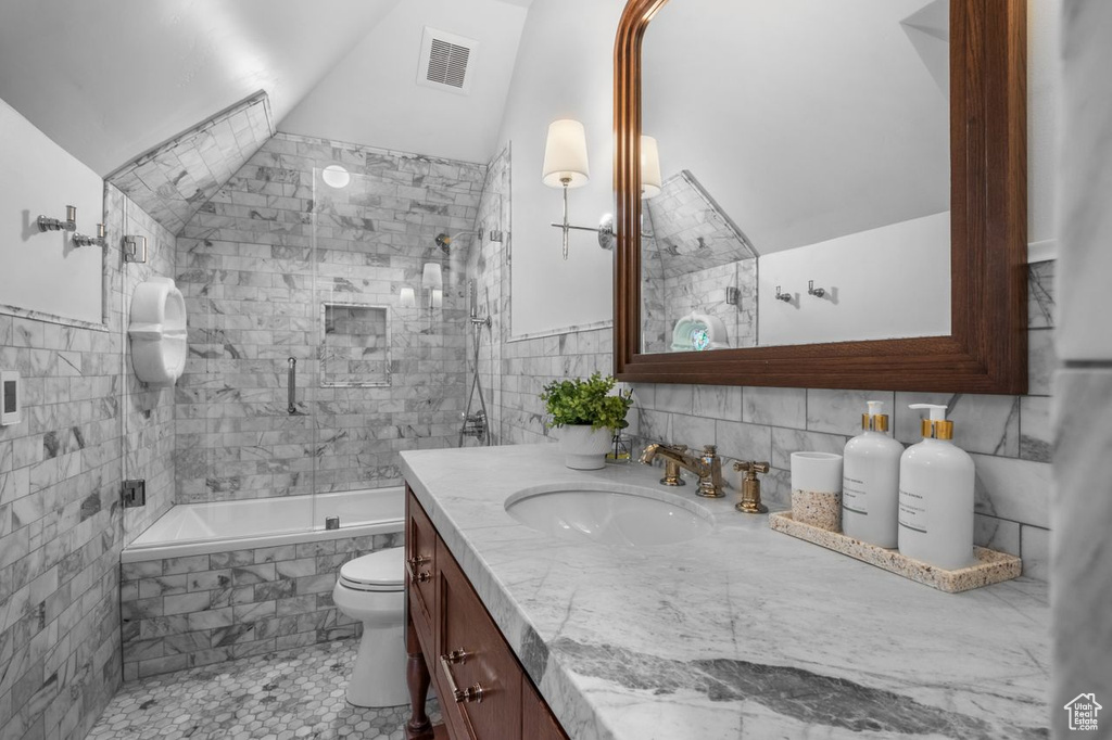 Bathroom with vanity, tile walls, tiled shower / bath combo, and lofted ceiling