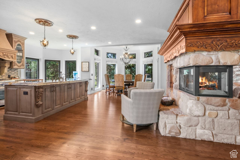 Living area featuring a stone fireplace, a chandelier, wood finished floors, and recessed lighting