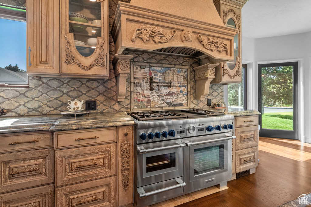 Kitchen featuring range with two ovens, dark wood-type flooring, premium range hood, tasteful backsplash, and glass insert cabinets