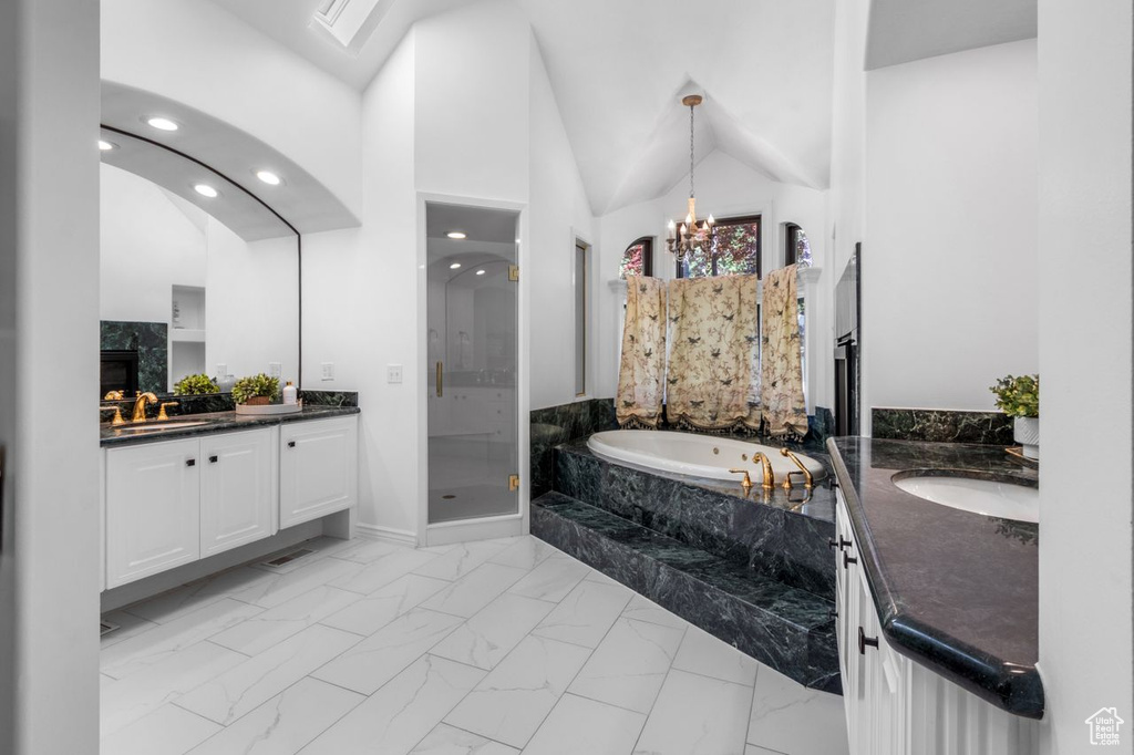 Full bathroom featuring marble finish flooring, two vanities, a bath, a shower stall, and a chandelier