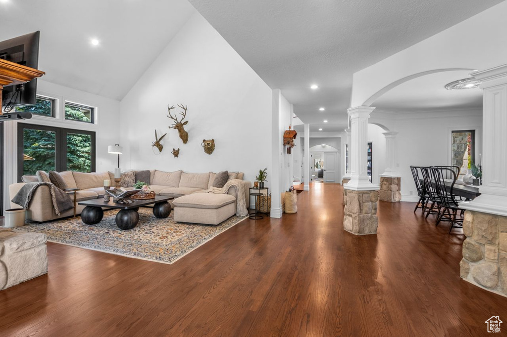 Living area featuring decorative columns, arched walkways, dark wood-style flooring, recessed lighting, and high vaulted ceiling