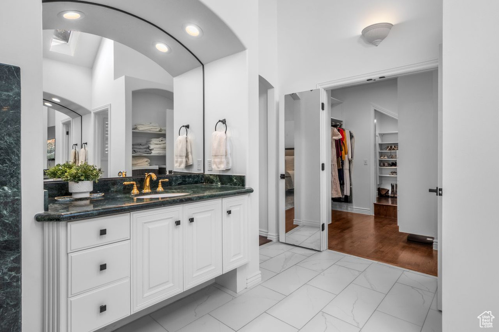 Bathroom with marble look tiles, vanity, a walk in closet, and recessed lighting