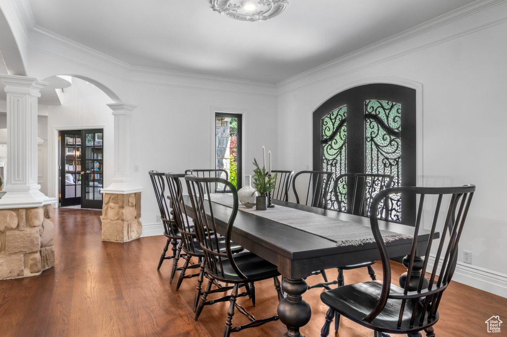 Dining room with ornate columns, arched walkways, ornamental molding, dark wood-style flooring, and french doors
