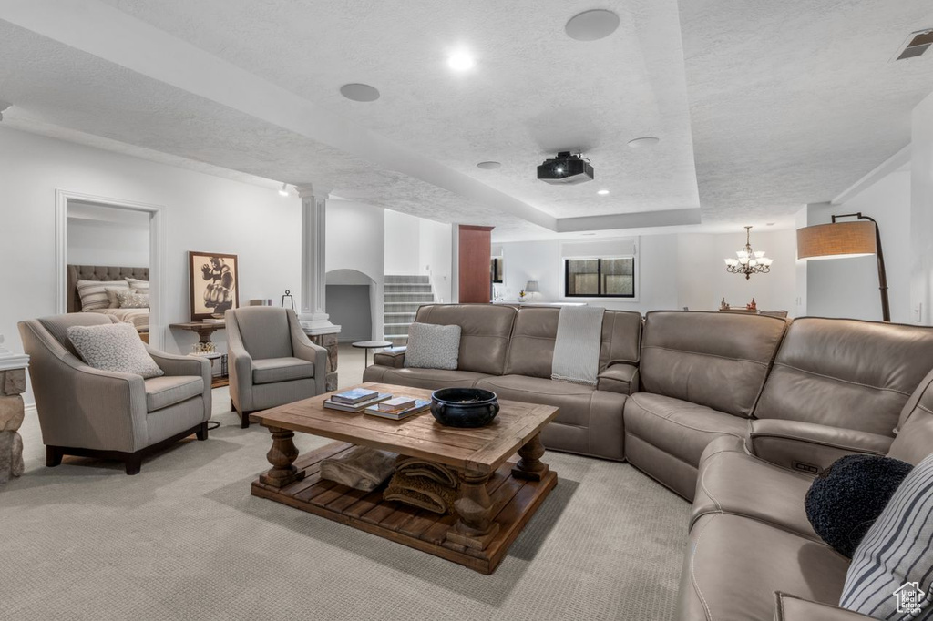 Living room featuring ornate columns, light colored carpet, a textured ceiling, a chandelier, and a raised ceiling