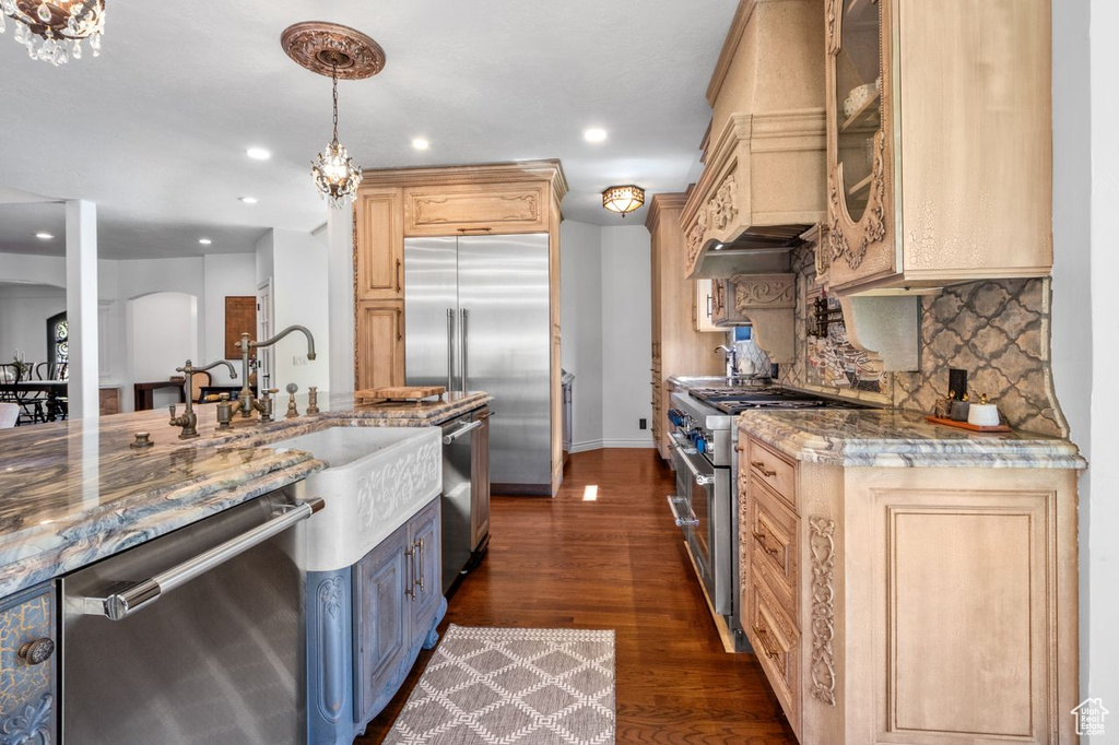 Kitchen with premium appliances, stone counters, dark wood-type flooring, backsplash, and recessed lighting