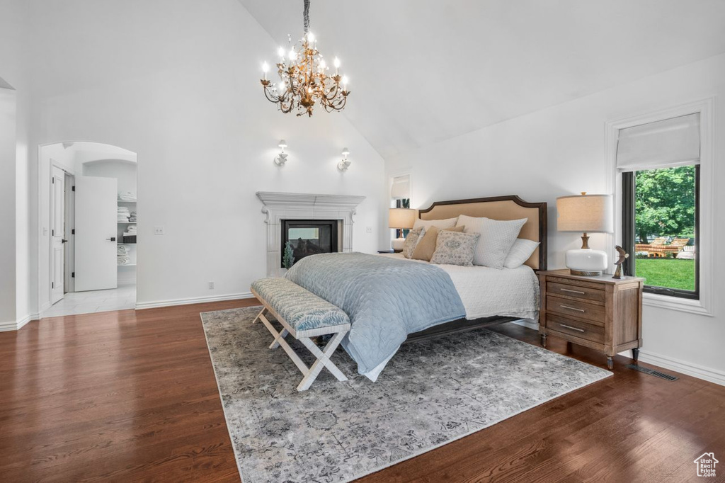 Bedroom featuring high vaulted ceiling, arched walkways, dark wood-style floors, a glass covered fireplace, and a chandelier