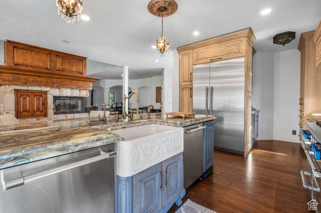 Kitchen with stainless steel appliances, arched walkways, dark wood finished floors, light stone counters, and a stone fireplace
