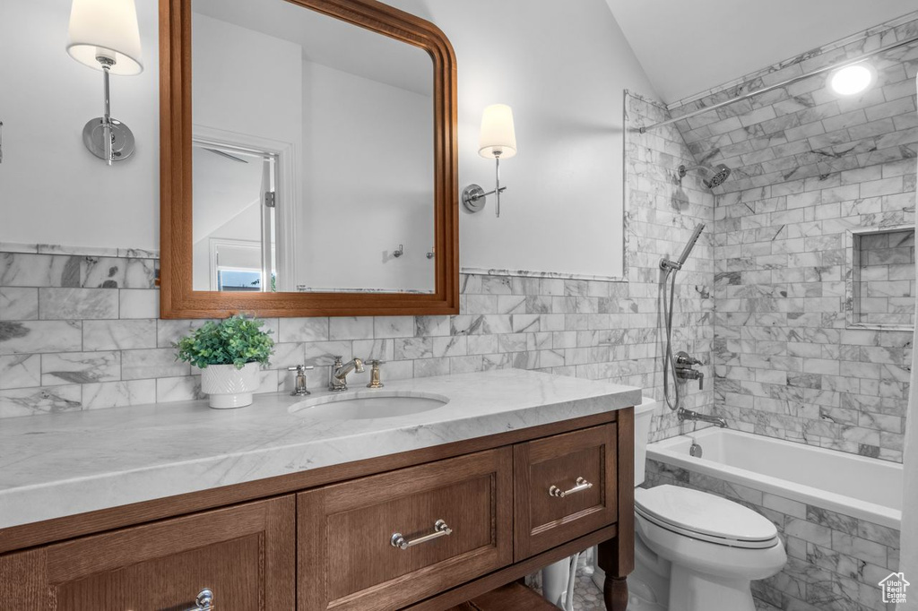 Full bathroom featuring vanity, tiled shower / bath combo, lofted ceiling, and tile walls