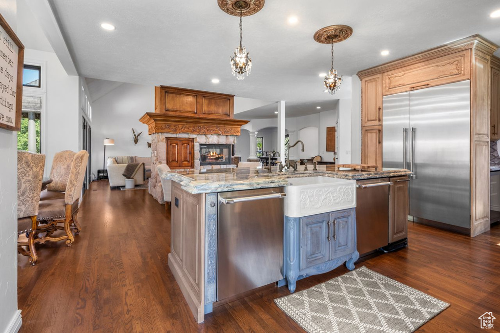 Kitchen with appliances with stainless steel finishes, open floor plan, a center island with sink, dark wood-type flooring, and light stone countertops