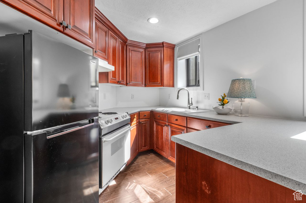 Kitchen with freestanding refrigerator, electric stove, light countertops, wood tiled floors, and under cabinet range hood