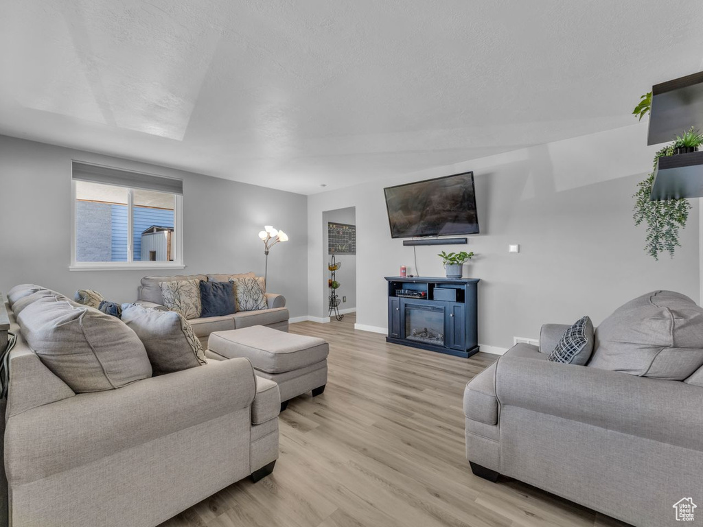 Living area with light wood-type flooring and a glass covered fireplace