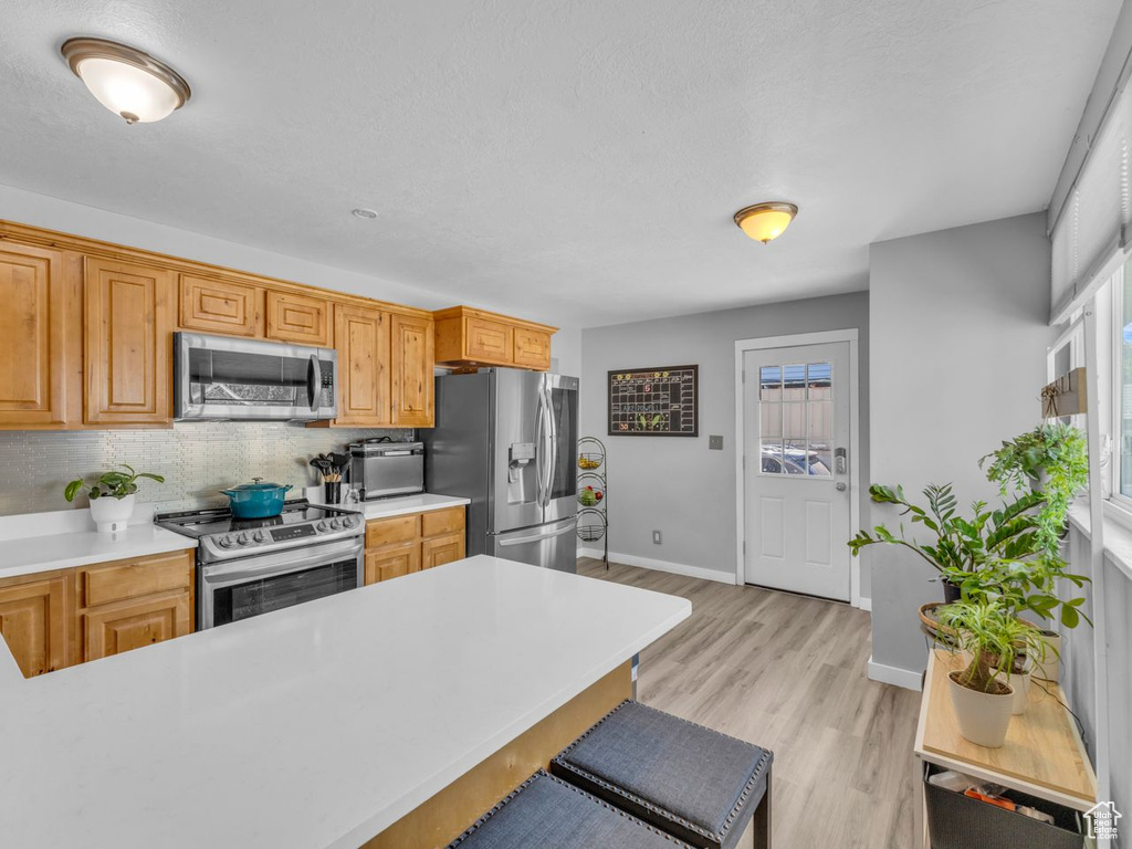 Kitchen with stainless steel appliances, light countertops, backsplash, light wood-type flooring, and a kitchen breakfast bar