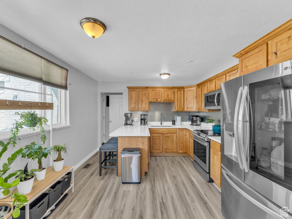 Kitchen with appliances with stainless steel finishes, light countertops, light wood finished floors, and decorative backsplash