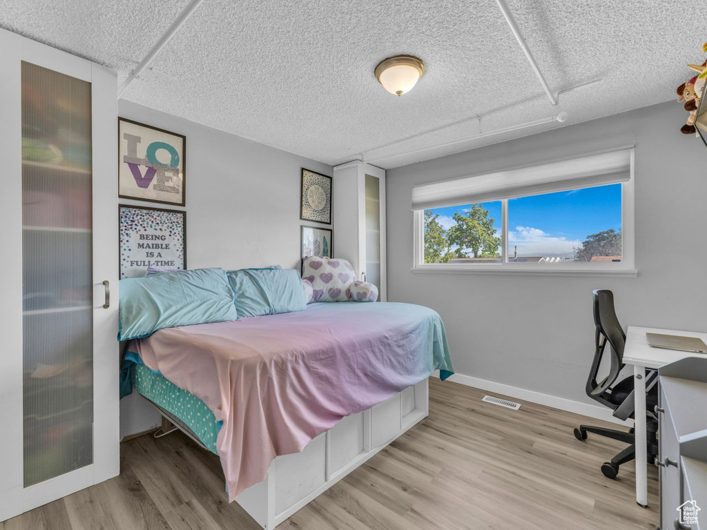 Bedroom with wood finished floors, a textured ceiling, and an office area
