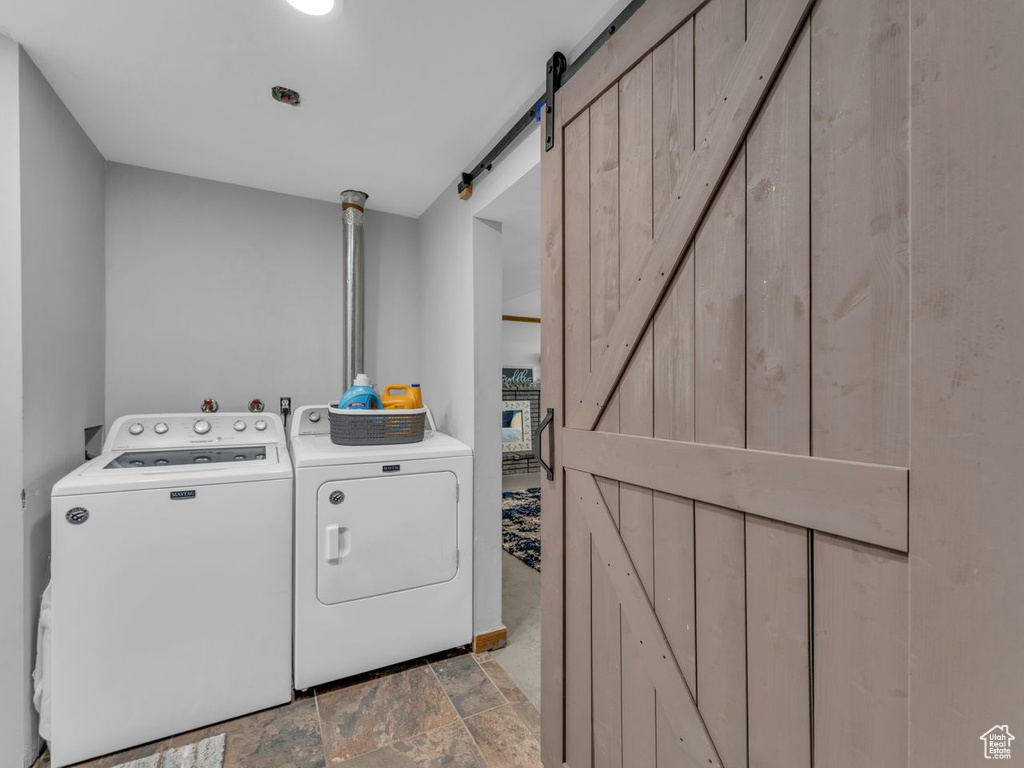 Laundry room with washing machine and dryer, a barn door, and light stone finish floors