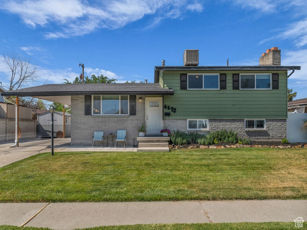 Tri-level home featuring a chimney, a shed, an attached carport, and a front lawn